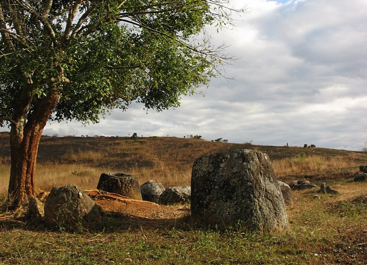Large carved stone jars scattered across a grassy hillside in northern Laos