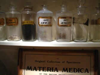 Antique glass medicine bottles on a shelf labeled Materia Medica in a historic apothecary garret