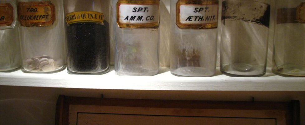 Antique glass medicine bottles on a shelf labeled Materia Medica in a historic apothecary garret