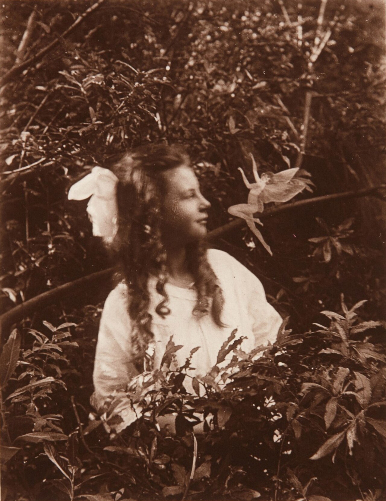 A black-and-white photograph of a young girl posing with tiny paper fairy figures