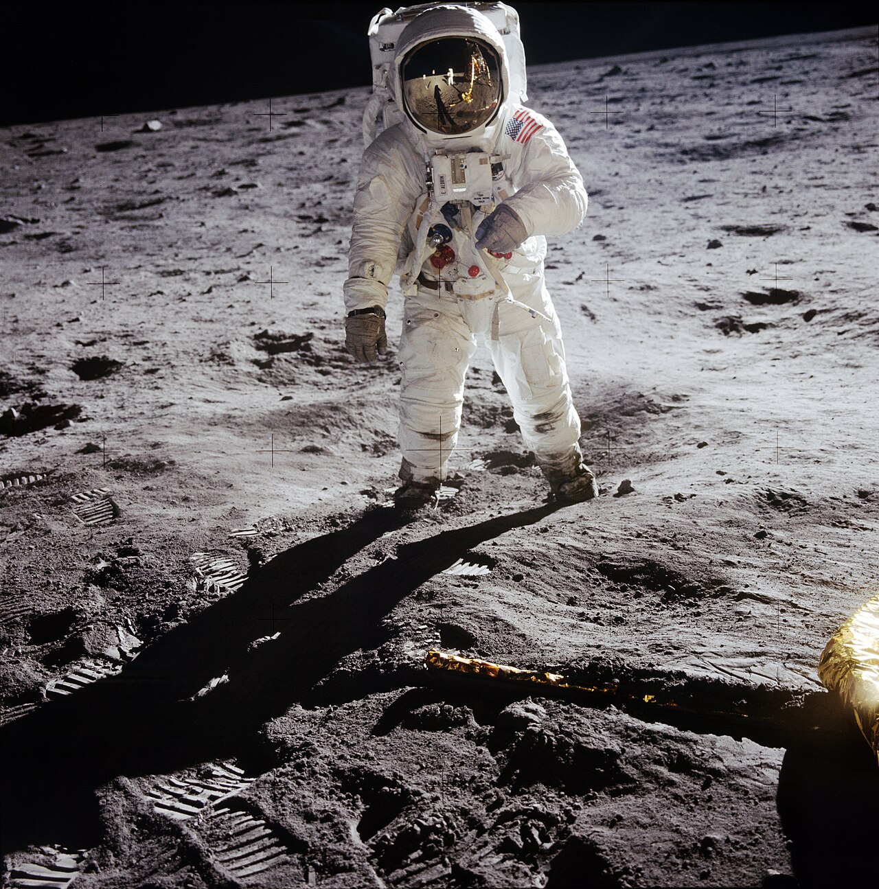 An Apollo 11 astronaut in a white spacesuit standing on the gray lunar surface