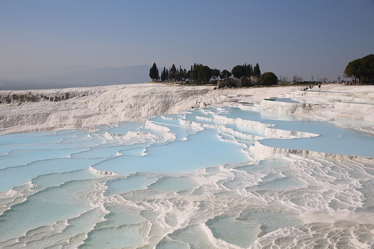 White travertine terraces holding pools of turquoise water on a hillside at Pamukkale