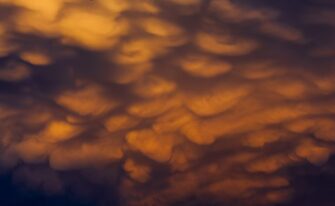 Glowing orange mammatus clouds bulging from the underside of a storm cloud
