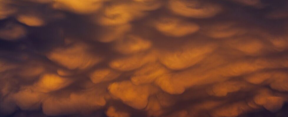 Glowing orange mammatus clouds bulging from the underside of a storm cloud