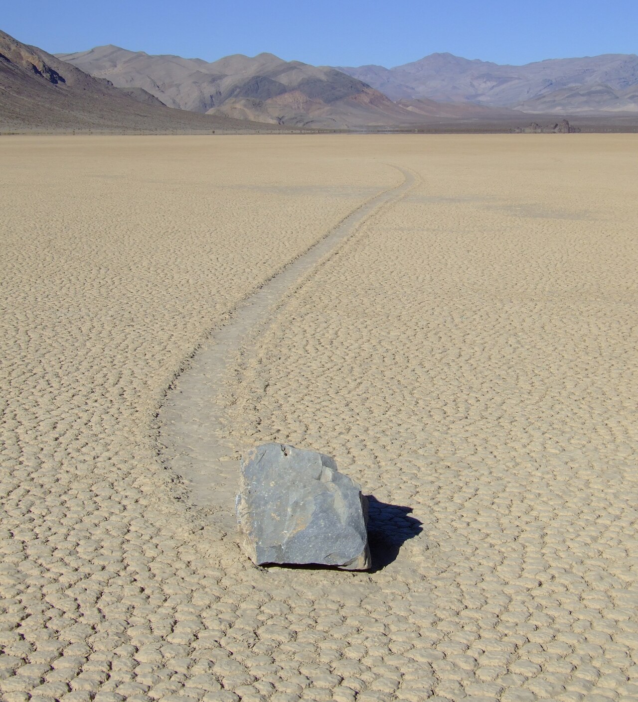 A rock resting at the end of a long trail on a cracked, dry lakebed