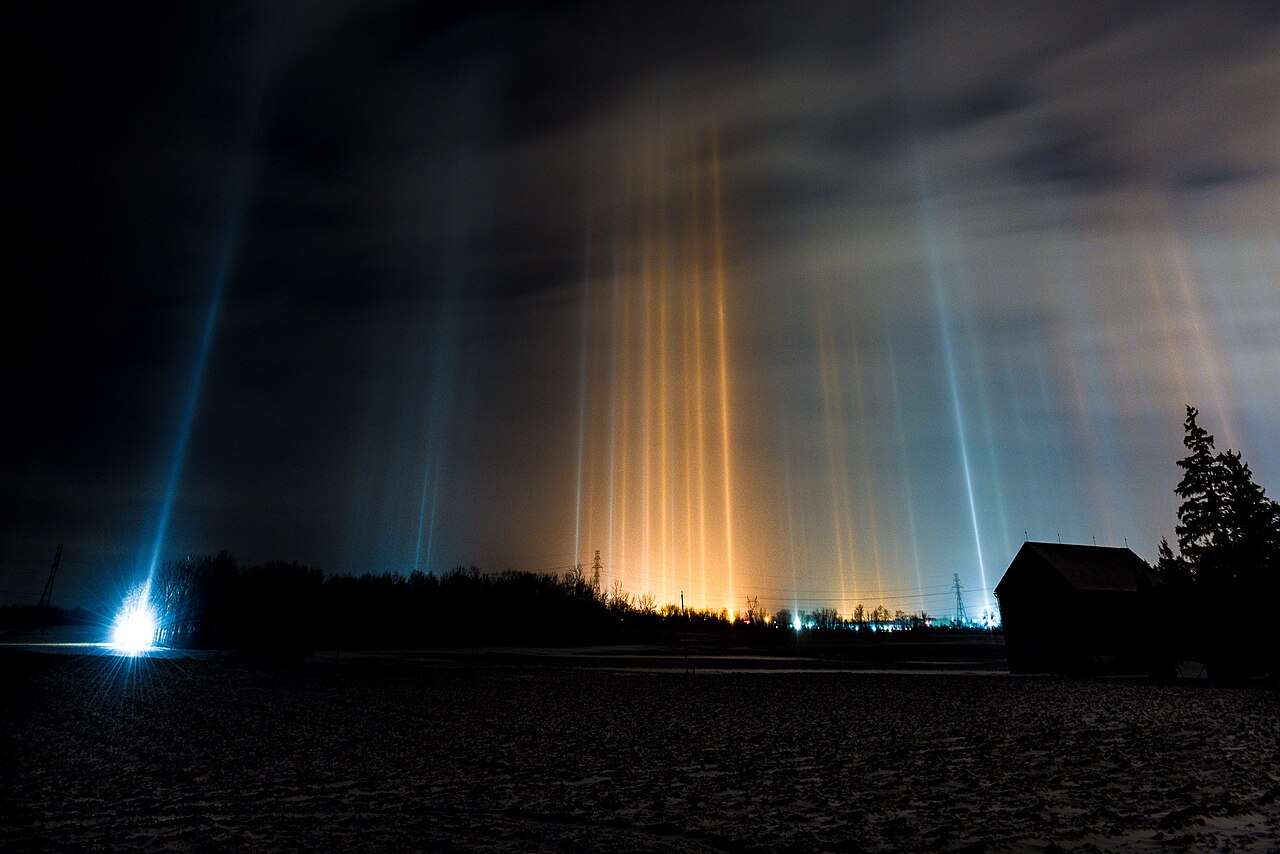 Vertical columns of light rising into a cold night sky above artificial lights