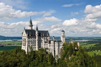 Neuschwanstein Castle with white walls and slender towers on a forested crag in the Alps