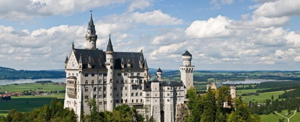 Neuschwanstein Castle with white walls and slender towers on a forested crag in the Alps