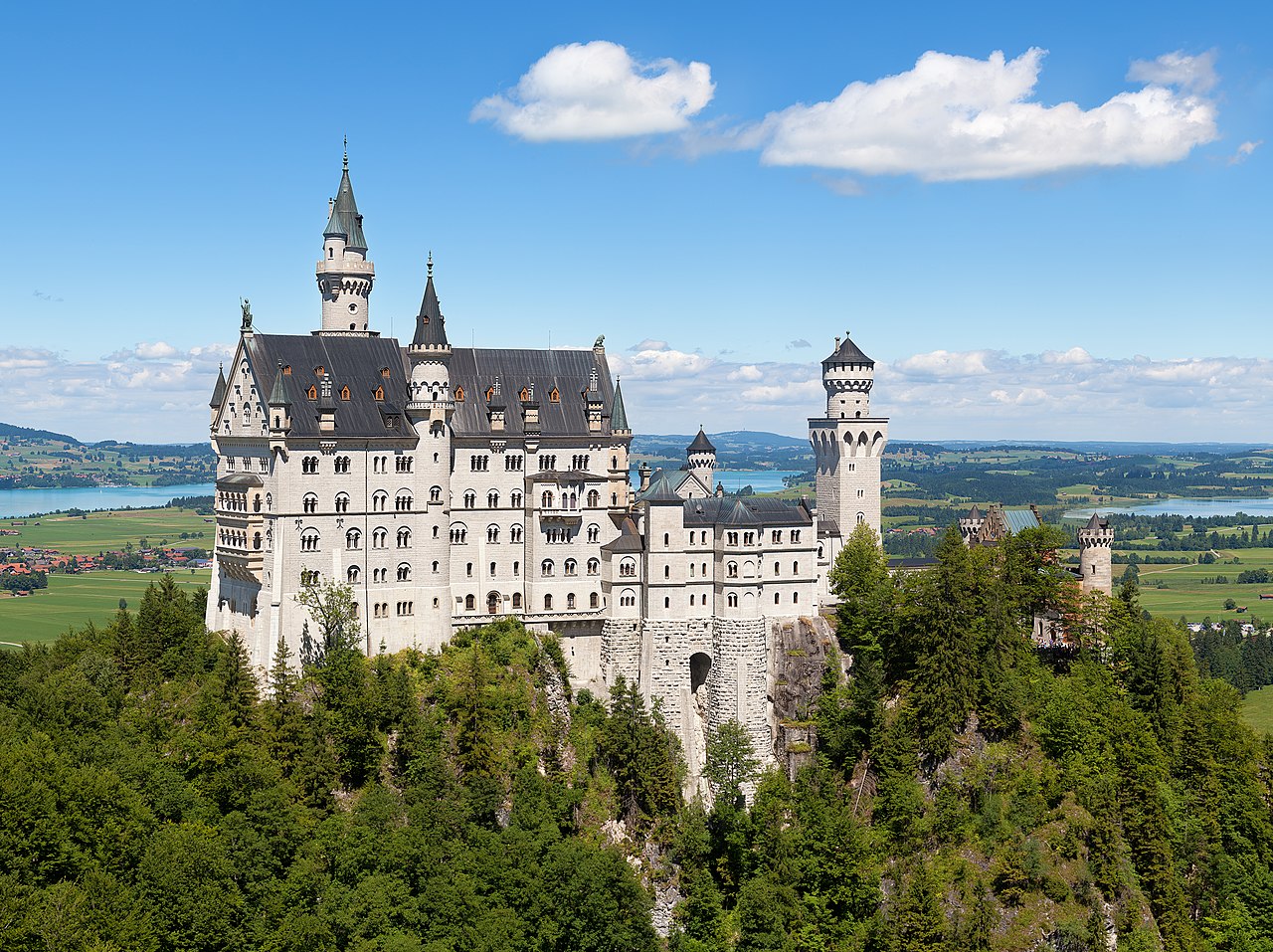 Neuschwanstein Castle with white walls and turrets on a crag above a forested gorge