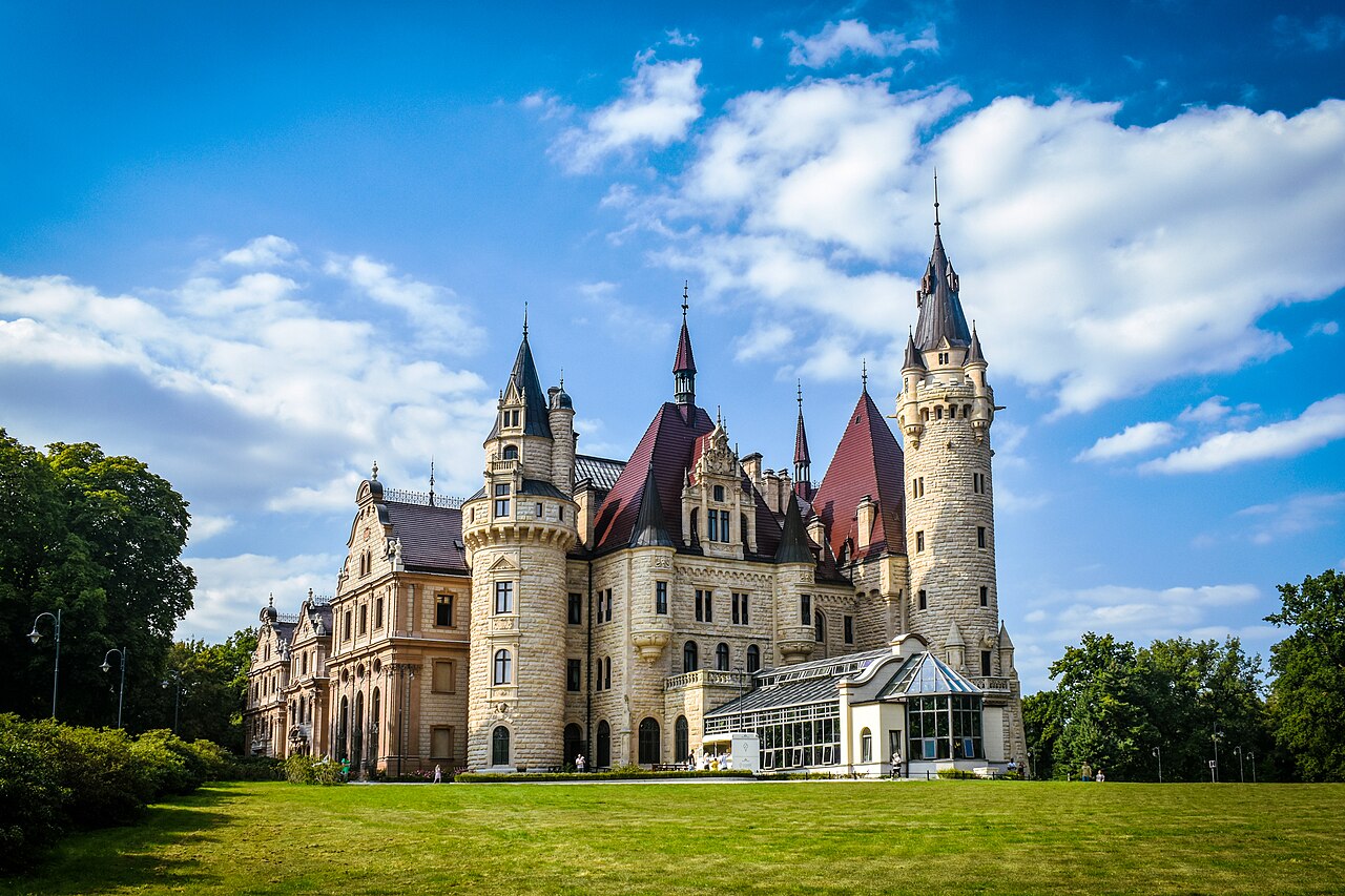 Moszna Castle in Poland with its many turrets, spires, and gables above a lawn