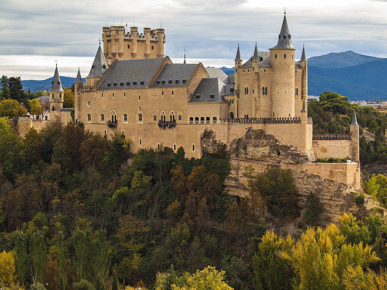 The Alcázar of Segovia with slate-roofed turrets on a rocky crag above trees